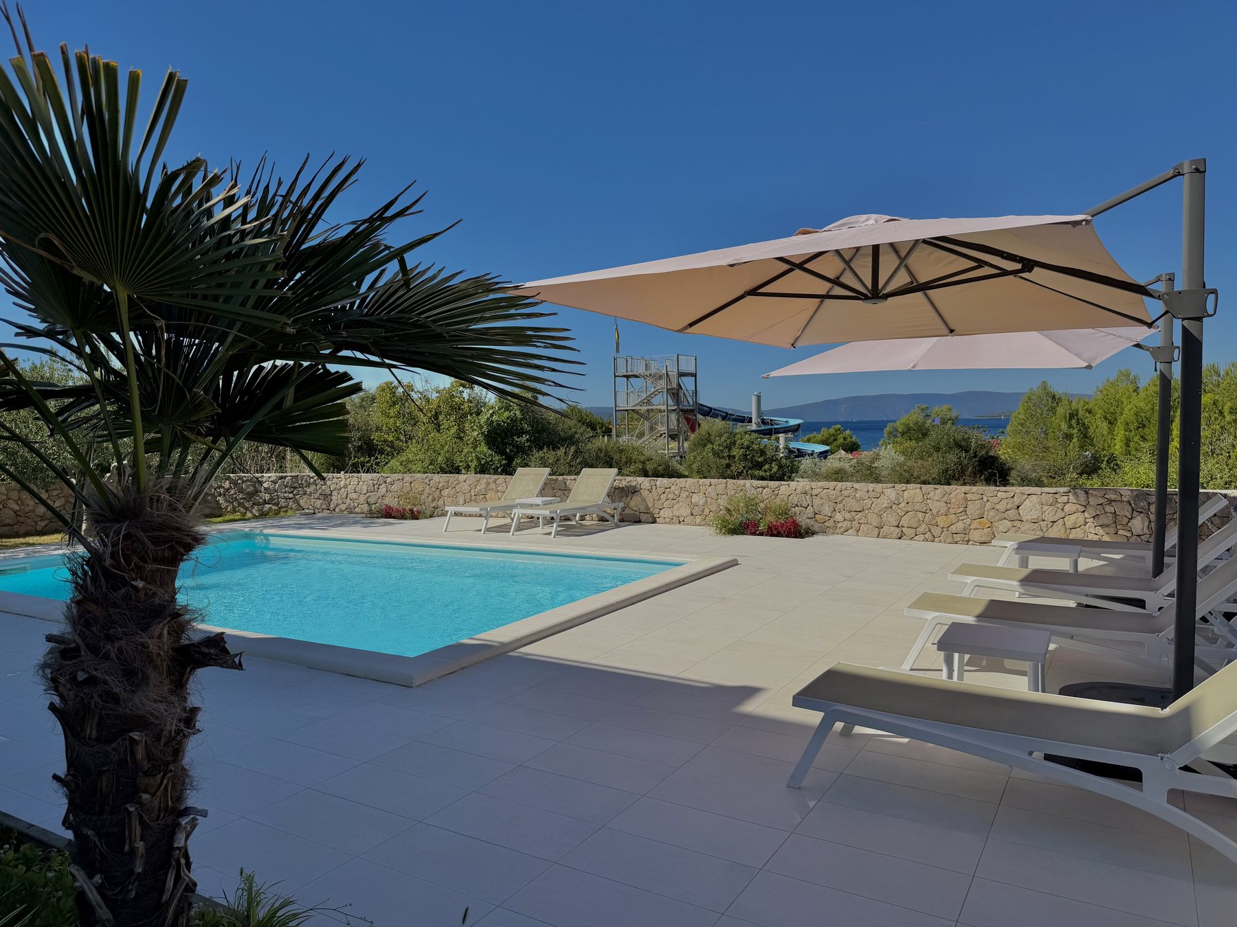 Pool with sun loungers and a parasol, sea view beyond